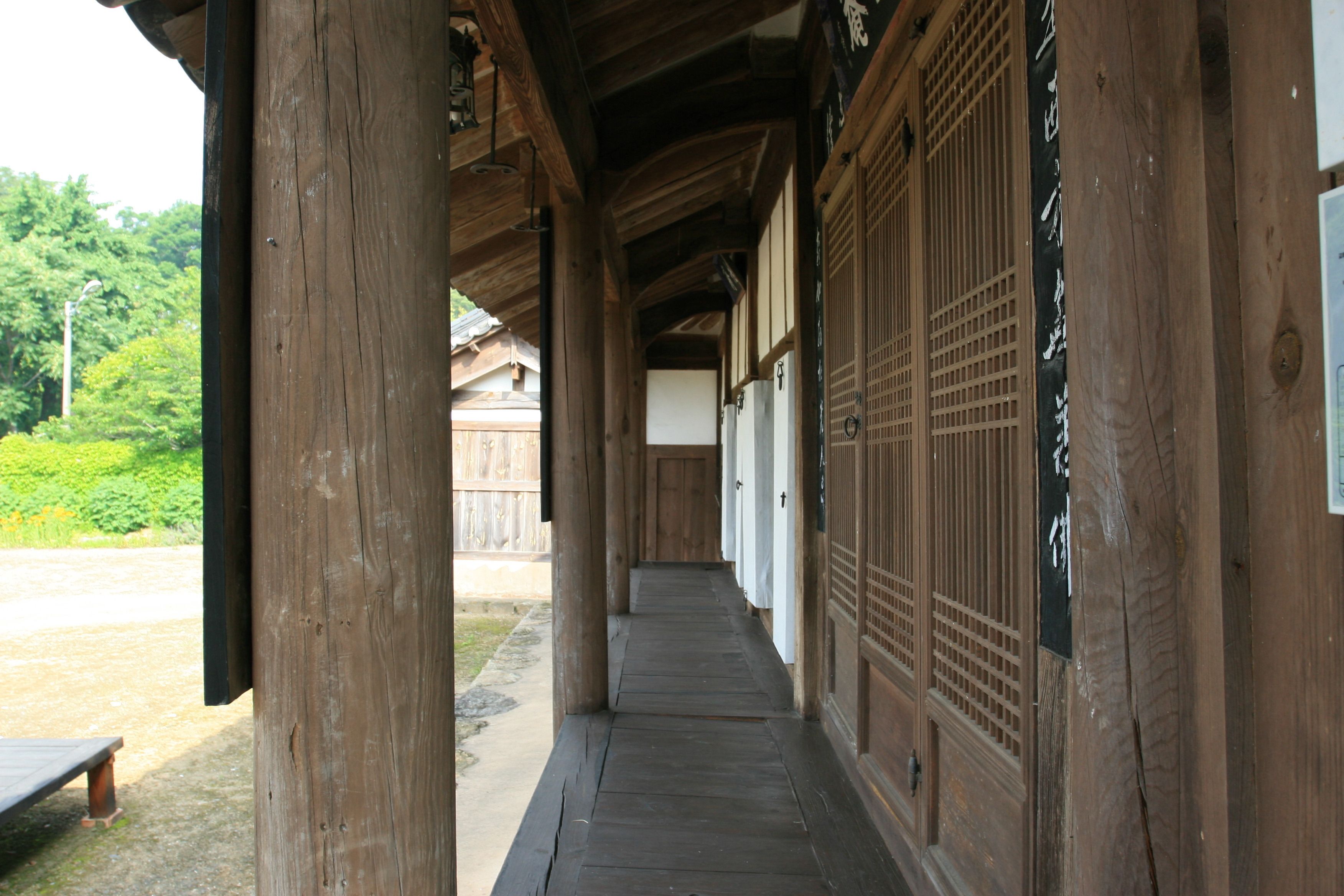 Een houten gang met traditionele Japanse deuren en een bankje erbuiten.