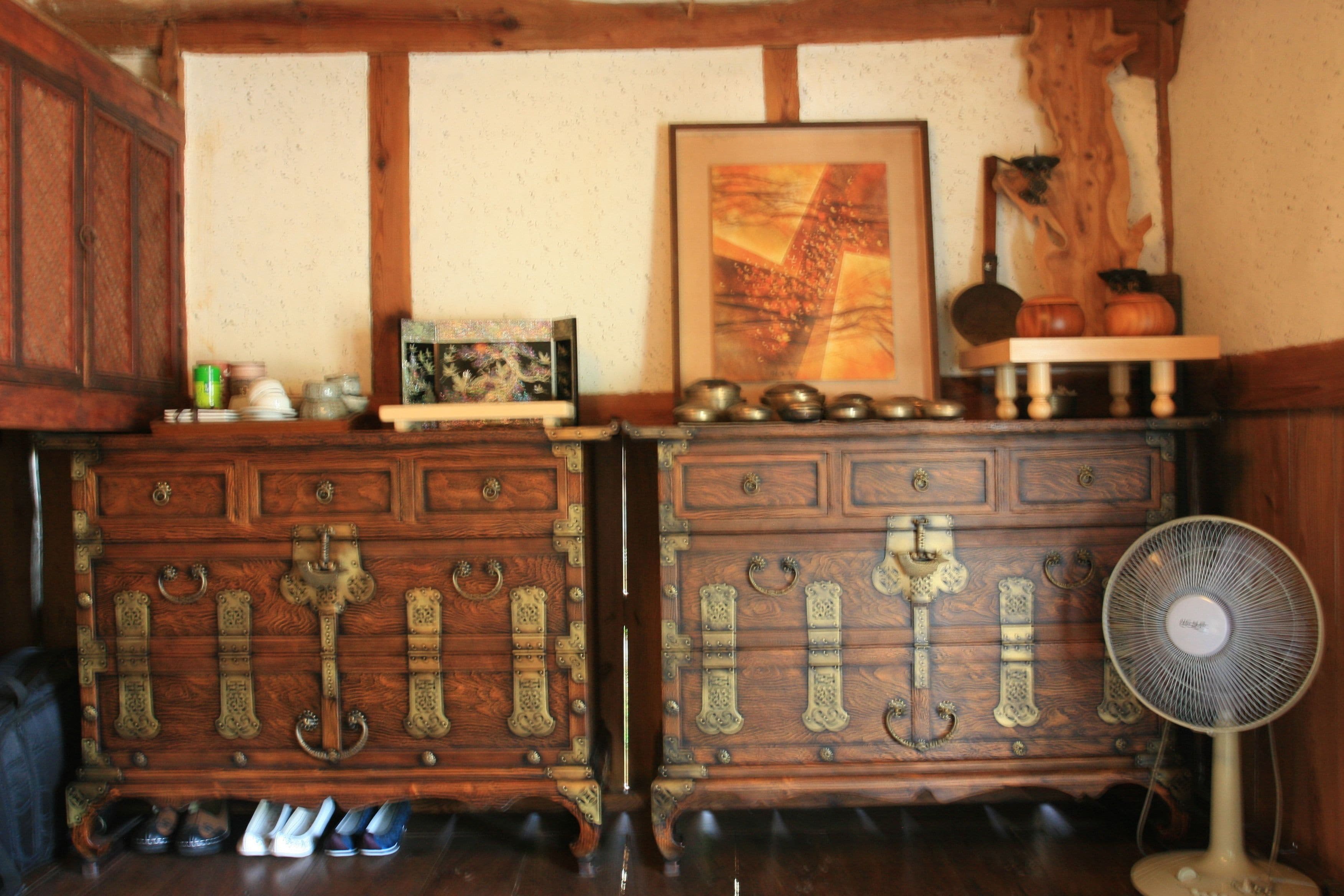 A wooden dresser with ornate metal handles and a fan on the right.