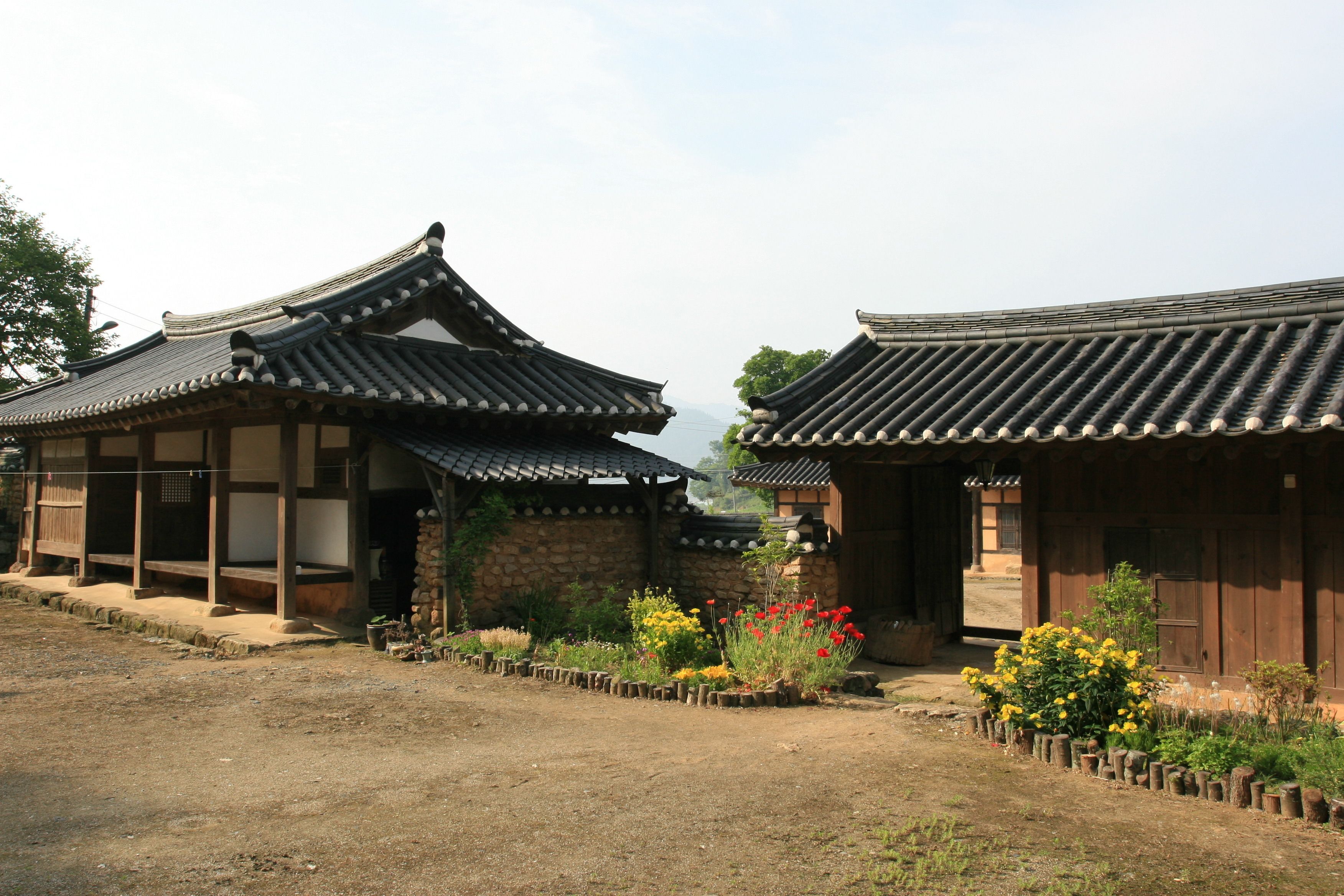 A traditional Korean-style building with a tiled roof and wooden structure, surrounded by a garden with various plants and flowers.