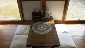 A wooden table with a lace doily, two white cushions, and a kettle on a wooden floor with a view outside. - Yi Jin-rae's Historic House (Boseong)
