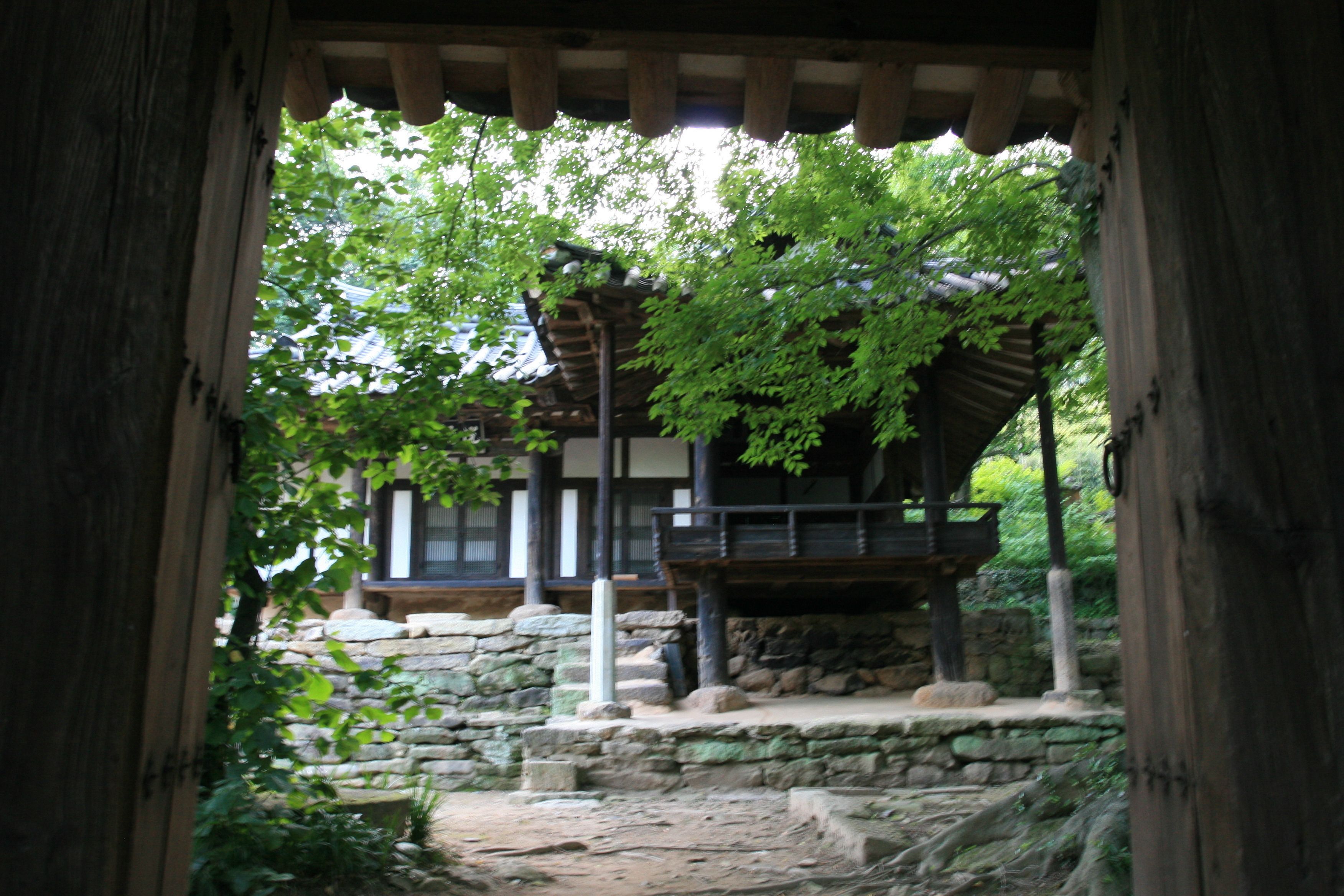 Une structure traditionnelle en bois, avec une base en pierre, entourée de verdure.