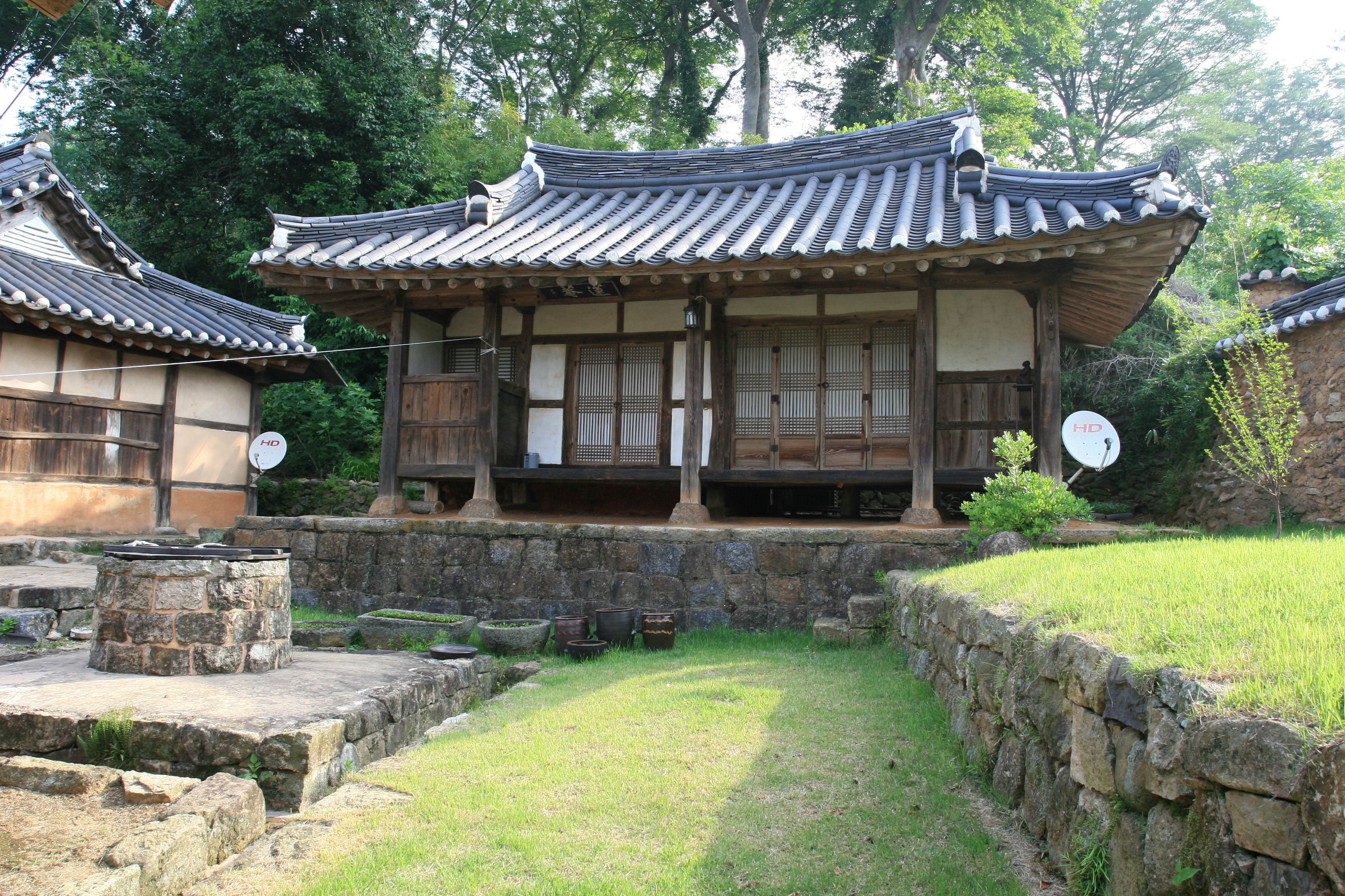 A traditional Korean building with a tiled roof, wooden beams, and a stone wall surrounding the courtyard.