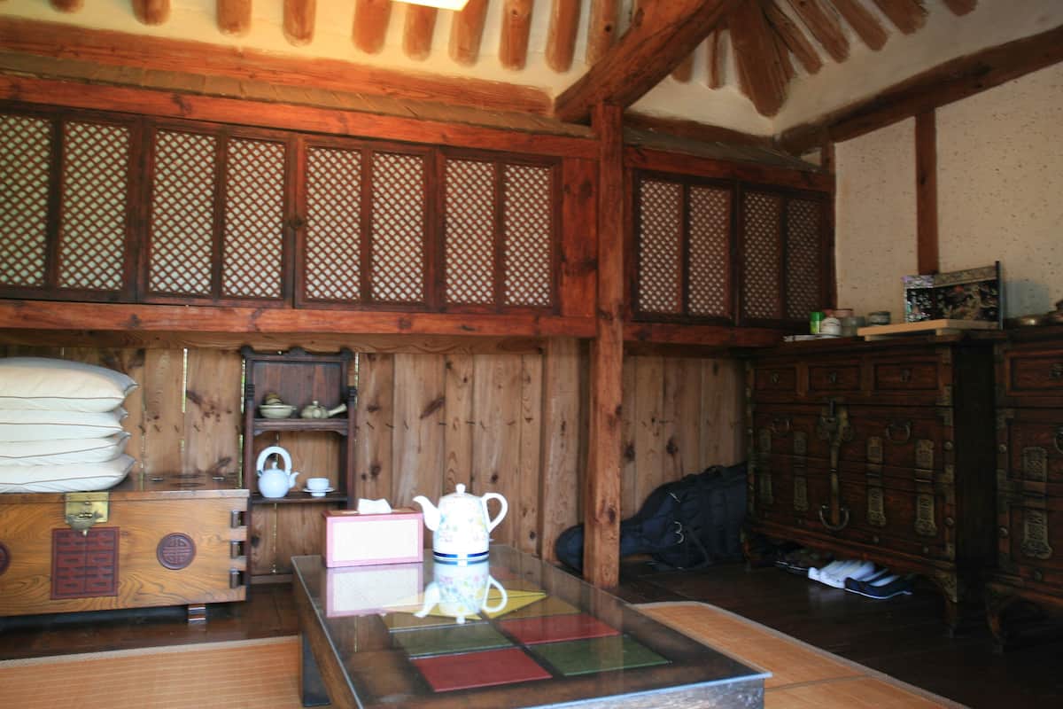 Een traditioneel houten interieur met tatami vloerbedekking, een lage tafel met theeservies en een houten kast met lades.