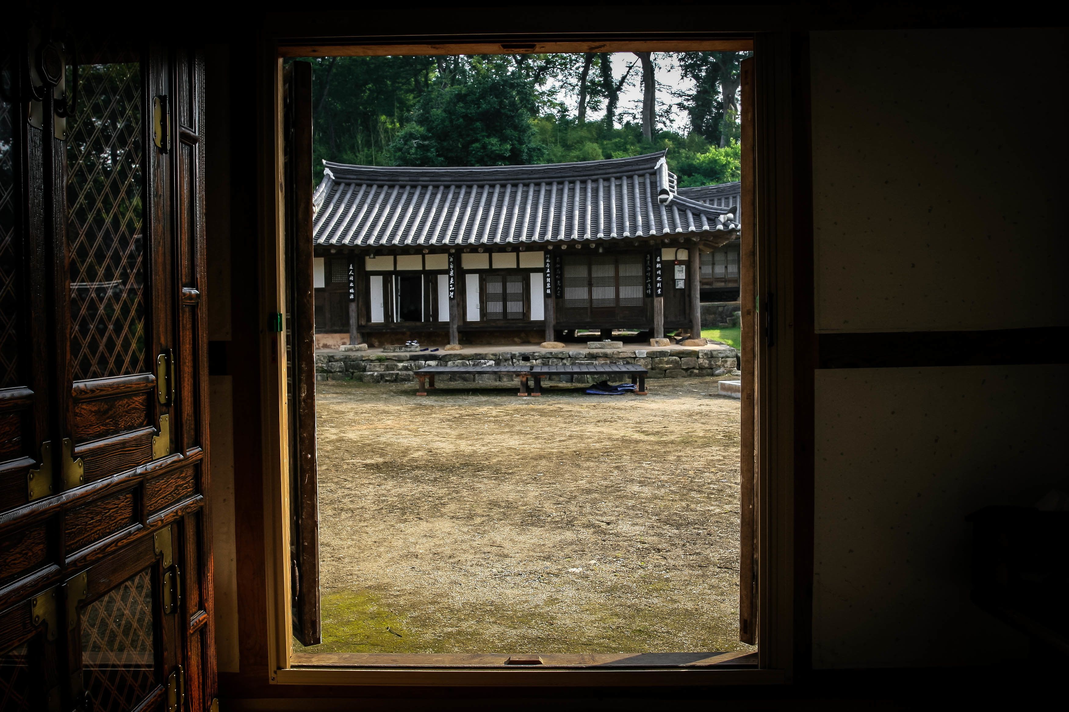 Um edifício japonês tradicional com telhado de telhas e estrutura de madeira, visto através de uma porta aberta.