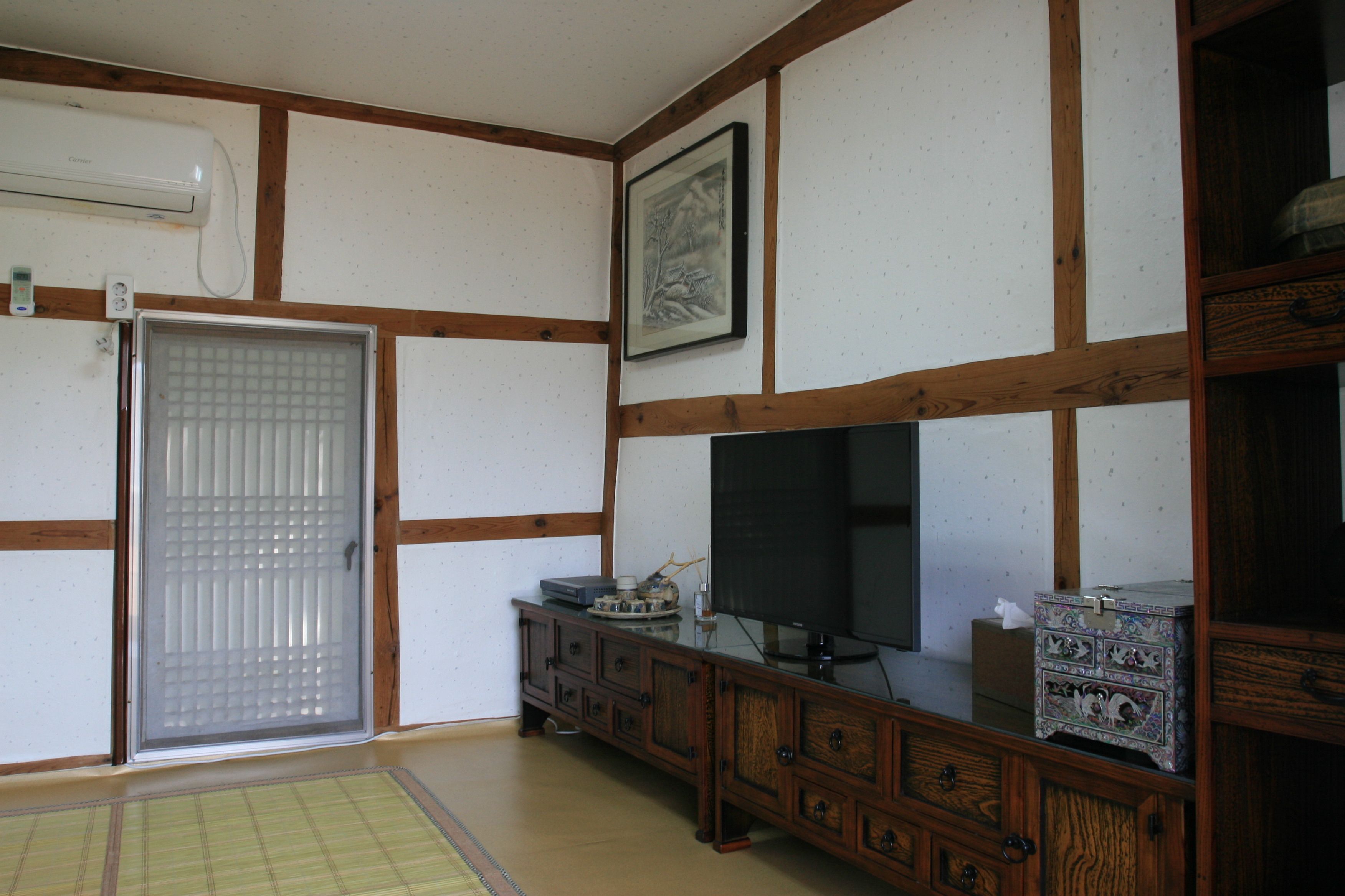 Ein traditioneller japanischer Raum mit Tatami-Böden, einer Schiebetür, einem Fernseher und einem Schrank mit Dekoration.
