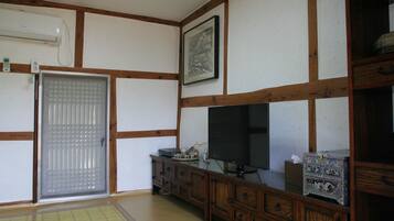 Ein traditioneller japanischer Raum mit Tatami-Böden, einer Schiebetür, einem Fernseher und einem Schrank mit Dekoration.