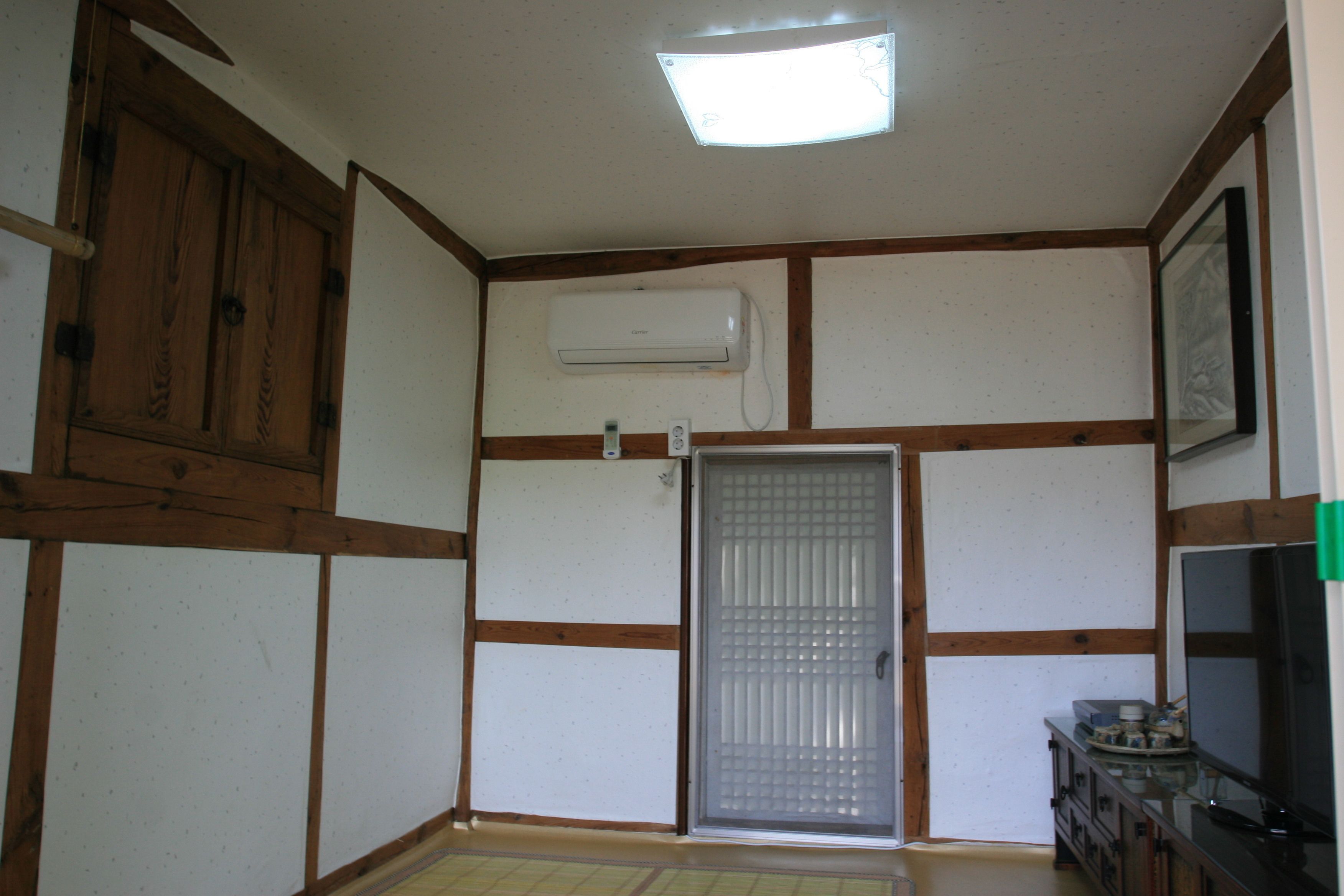 Una habitación con paneles de madera, una puerta corredera, un ventilador de techo, aire acondicionado instalado y un televisor.