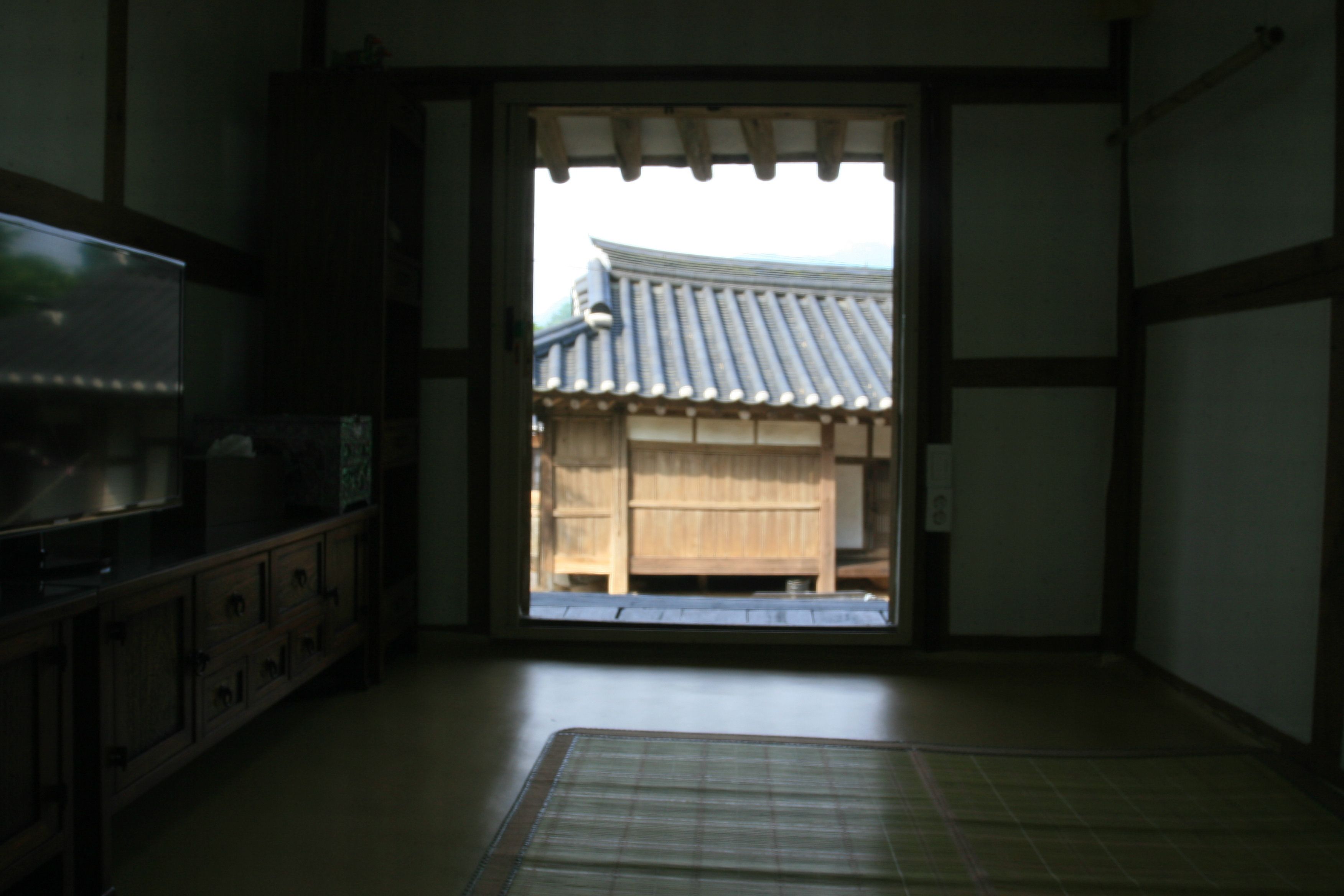 Ein traditioneller japanischer Raum mit Tatami-Boden, einer Schiebetür zu einer Holzwand und einem Fernseher auf einem Schrank.