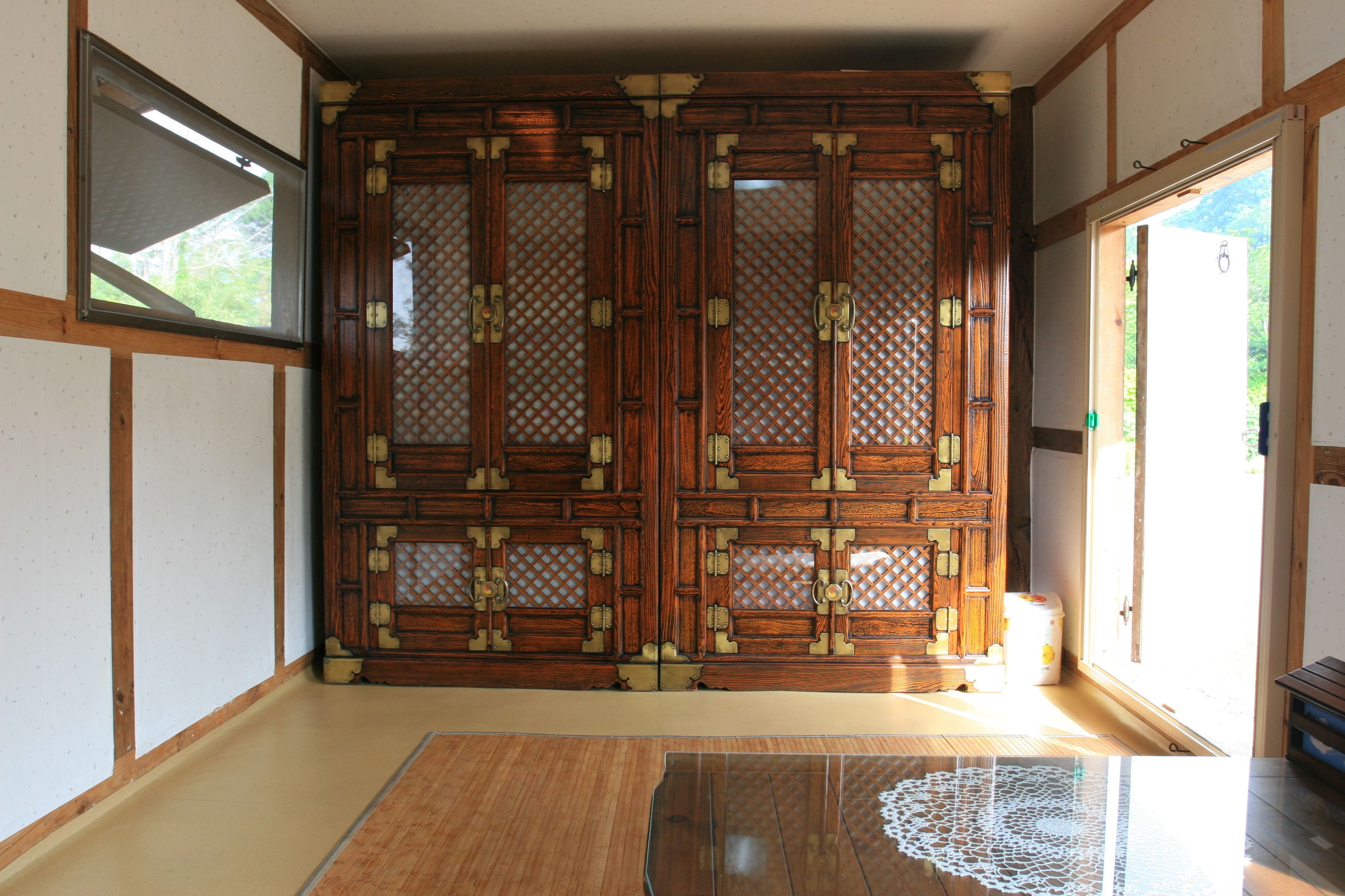 Una habitación tradicional japonesa con suelo de tatami, puertas correderas con intrincados detalles de madera y una mesa de cristal con un mantel de encaje.