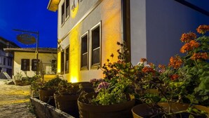 A building with a signboard, potted plants, and a cobblestone street at night. - Akcasu Konuk Evi (Safranbolu)