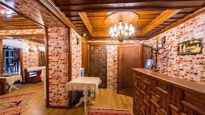 A traditional inn with brick walls, wooden floors, a chandelier, and a reception area with a sign. - Akcasu Konuk Evi (Safranbolu)