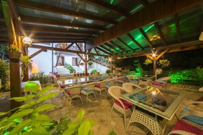 An outdoor patio area with wicker furniture, a glass-top table, and hanging planters. - Akcasu Konuk Evi (Safranbolu)
