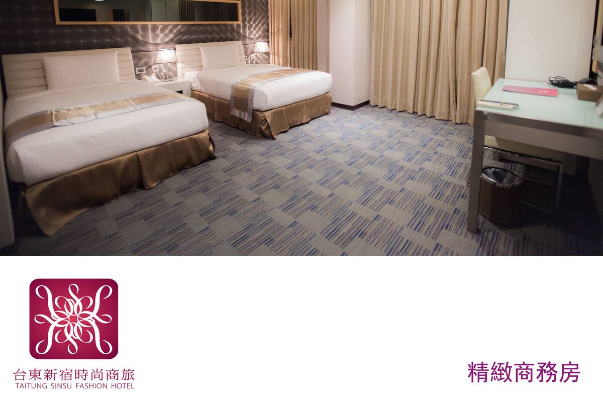A hotel room with two beds, a desk, a mirror, and a window with curtains.