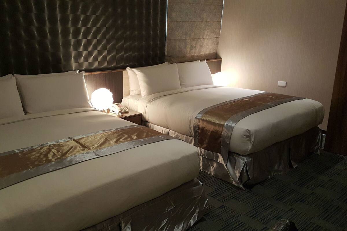 A hotel room with two beds, a headboard, bedside tables, and a lamp.
