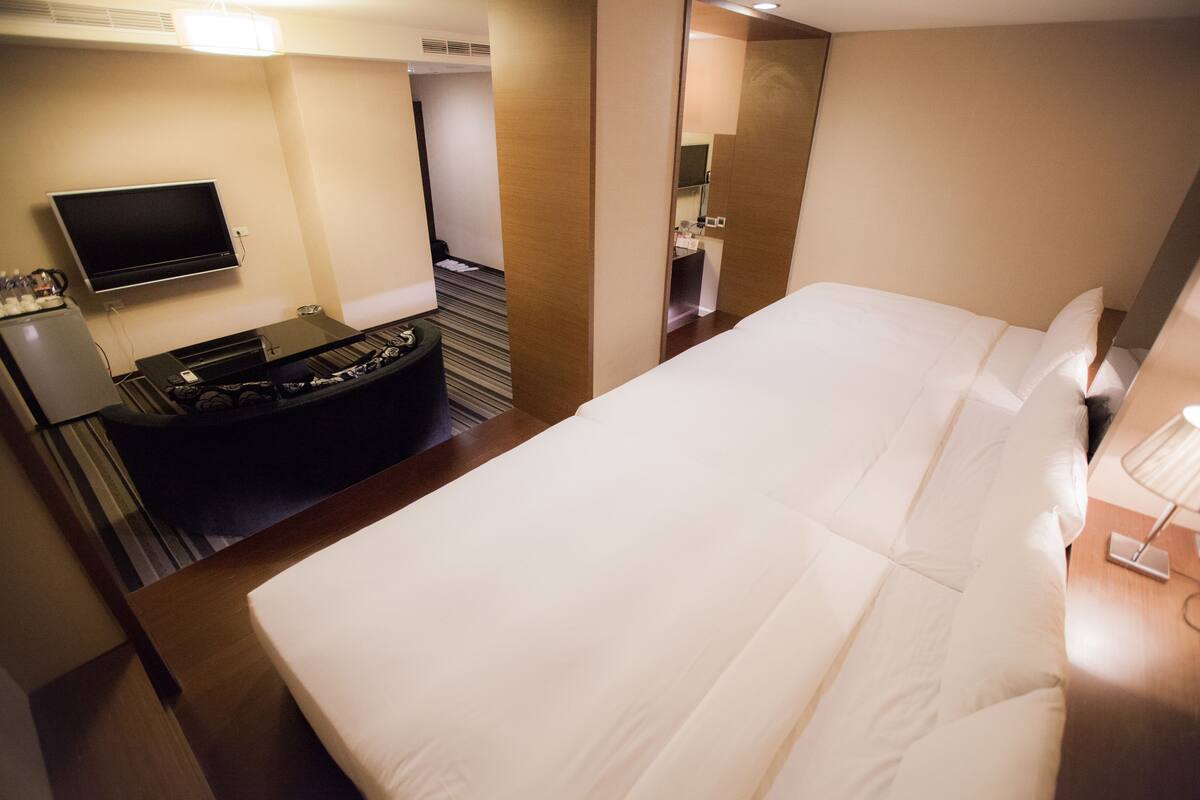 A hotel room with a bed, a TV, a desk, and a small kitchenette.