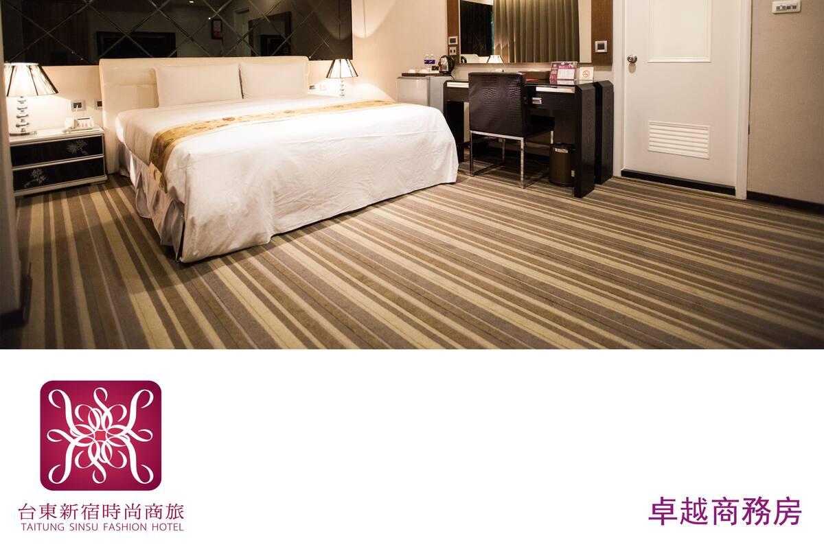 A hotel room with a bed, desk, and chair, a mirror, and a door.