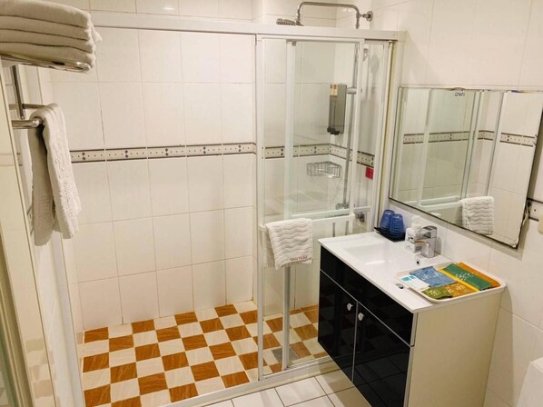 A hotel bathroom with a glass shower enclosure, a sink with toiletries, and a mirror. - Kai Shen Sinsu Hotel (Taitung)