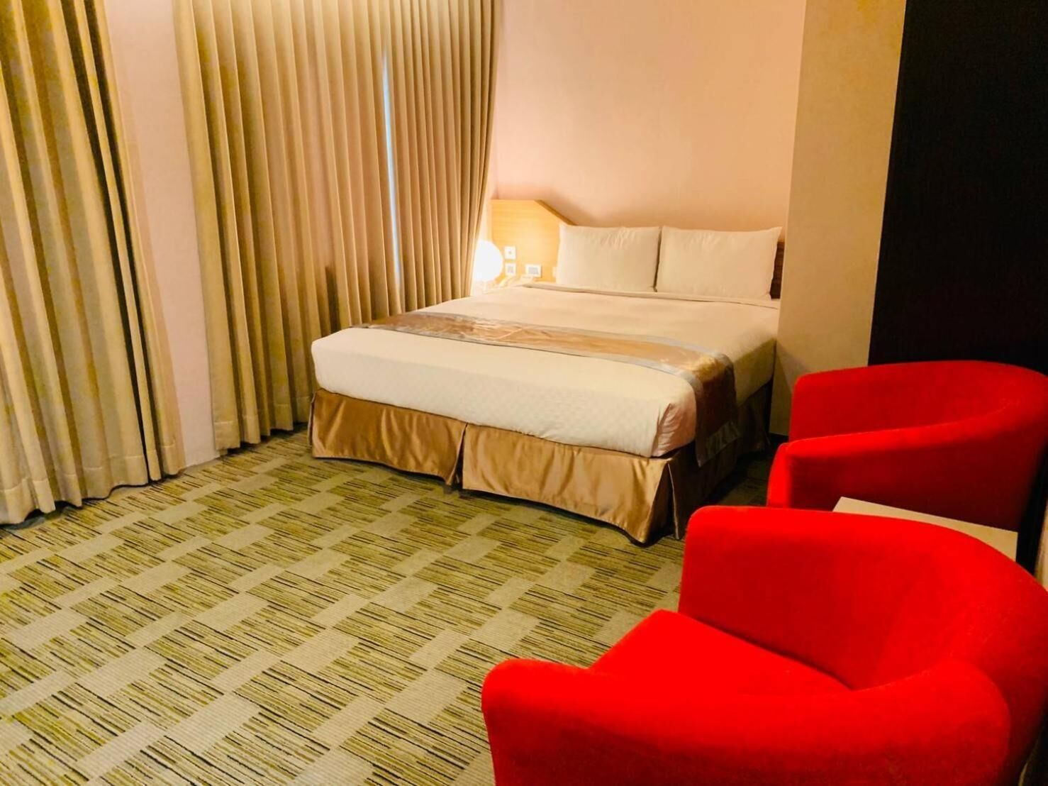 A hotel room with a bed, a red armchair, and a patterned carpet.