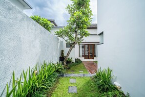 A modern house with a narrow front yard, a small tree, and a pathway leading to the entrance. - The Dewi Pererenan Villa and Suite (Canggu)