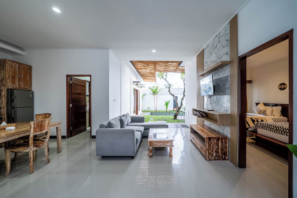Una sala de estar moderna con un sofá gris, una mesa de comedor de madera y un televisor montado en una pared de mármol.