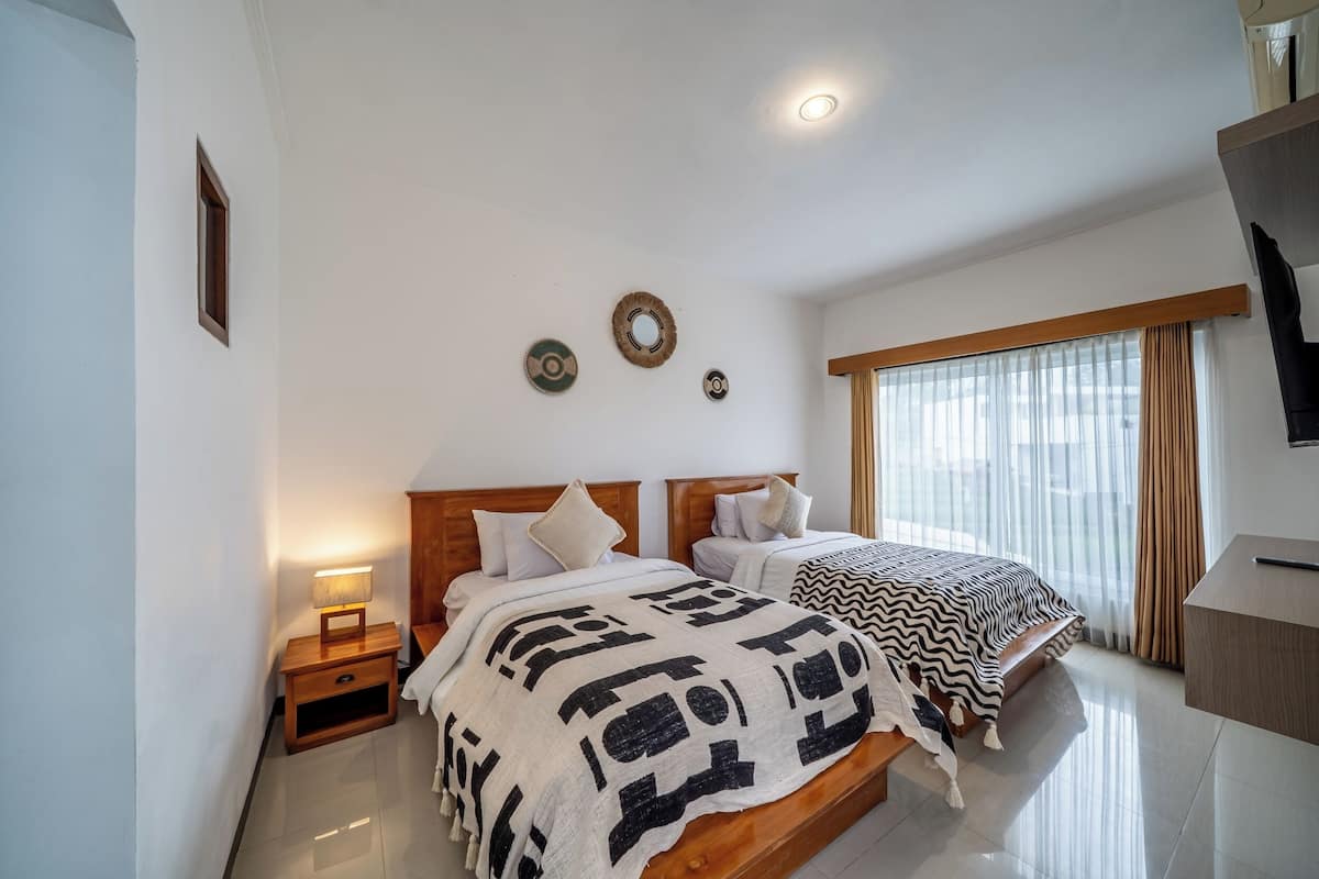 Un dormitorio con dos camas, una mesita de noche, un escritorio y una ventana con cortinas.