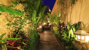 A narrow pathway flanked by lush greenery and a stone lantern, leading to a building entrance. - The Dewi Pererenan Villa and Suite (Canggu)