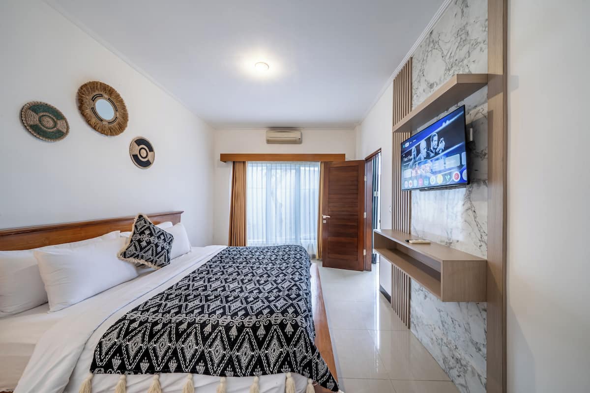 Habitación de hotel con una cama, un televisor montado en la pared, cabecera de madera y una puerta que da a otra habitación.