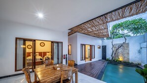 A modern interior with a dining area, a pool, and a bedroom with sliding doors. - The Dewi Pererenan Villa and Suite (Canggu)