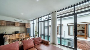 A modern living room with a brown leather sofa, a dining area with wooden furniture, and large sliding glass doors leading to a pool area. - The Dewi Pererenan Villa and Suite (Canggu)