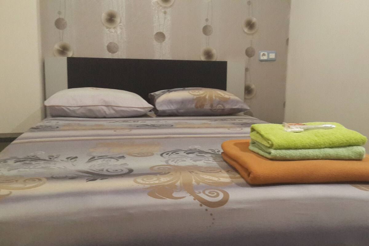 A neatly made bed with patterned bedding, pillows, and folded towels.