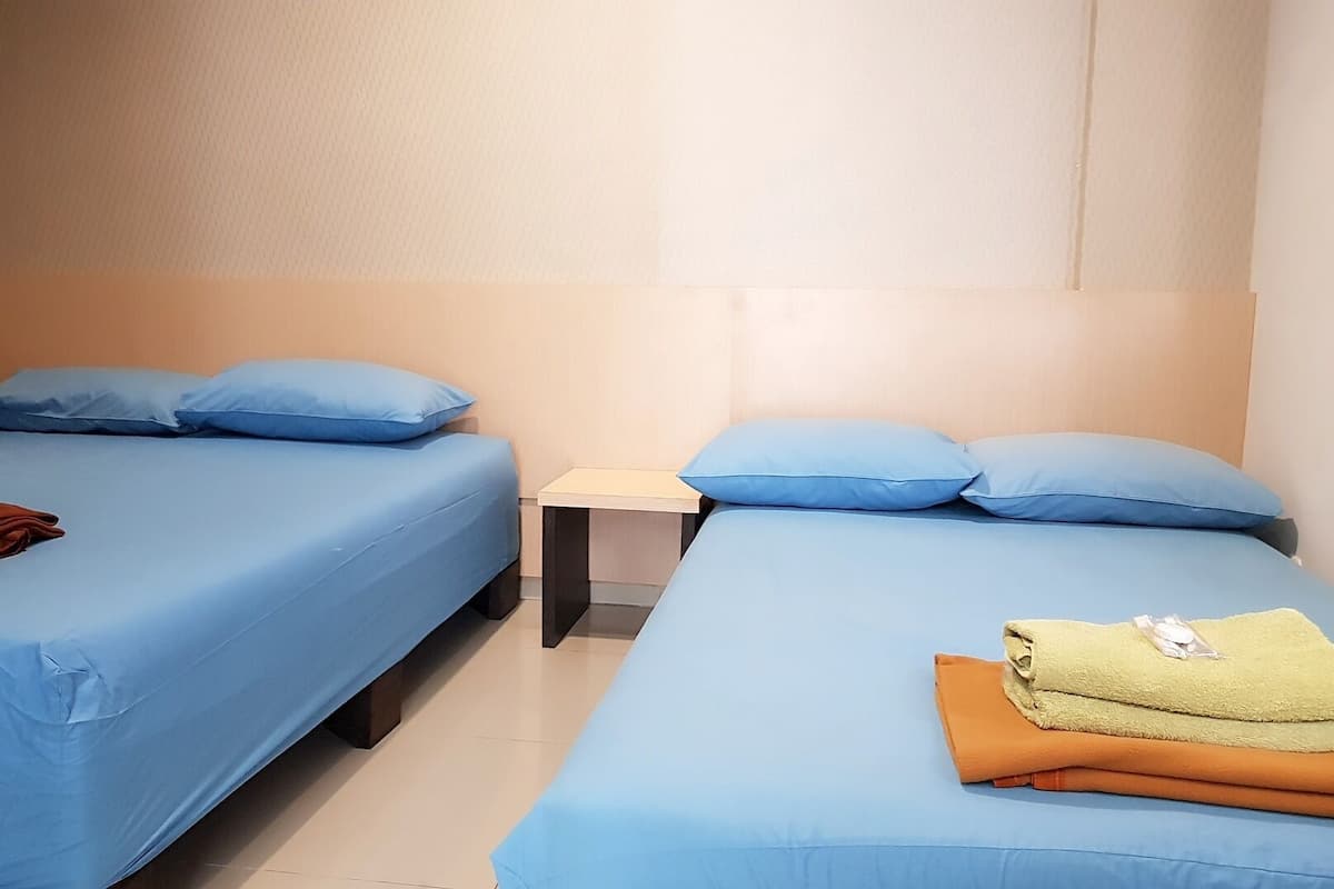 A hotel room with two single beds, each with blue bedding and pillows, a small bedside table, and a curtain with a circular pattern.