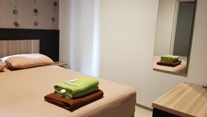 A hotel room with a bed, a bedside table, a mirror, and a window with curtains. - iHome Residence (Jakarta)