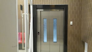 An elevator door with a control panel and a light switch on the wall. - iHome Residence (Jakarta)