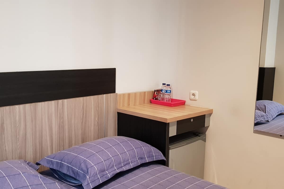 A hotel room with two beds, a wooden headboard, a small desk with a red tray, and a mirror on the wall.
