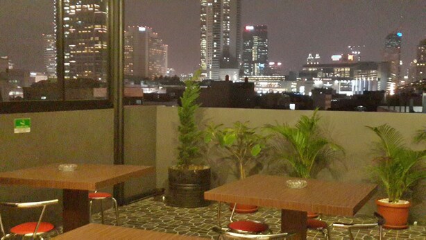 A rooftop terrace with tables and chairs, potted plants, and a city skyline view at night. - iHome Residence (Jakarta)