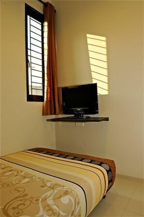 A bedroom with a bed, a television on a stand, a window with curtains, and a wall-mounted shelf. - iCorner Residence (Jakarta)