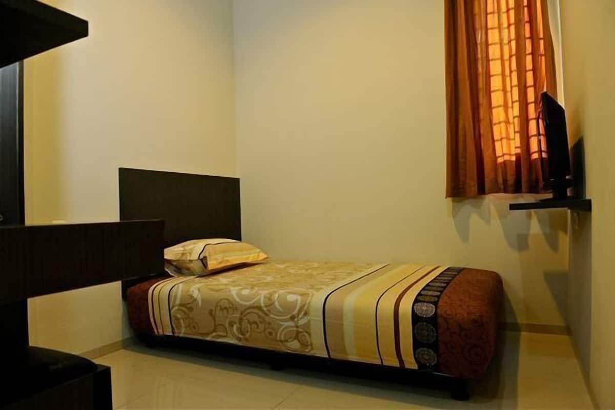 Une petite chambre à coucher, bien rangée, avec un lit, une table de chevet et un téléviseur posé sur un meuble.