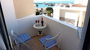 Un balcón con dos sillas y una mesita, con vistas a un puerto deportivo y al mar.