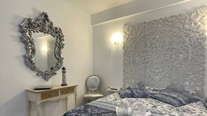 Un dormitorio con cama, mesita de noche, espejo y un muro con paneles decorativos.