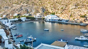 Un pueblo costero con edificios blancos, un muelle y varias embarcaciones, sobre terreno rocoso.