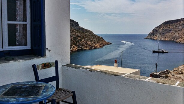 Un balcón con mesa y silla, con vista a una zona costera con un bote y acantilados.