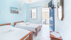 Una habitación con dos camas de madera, un ventilador de techo, un televisor montado y una puerta que da al exterior.