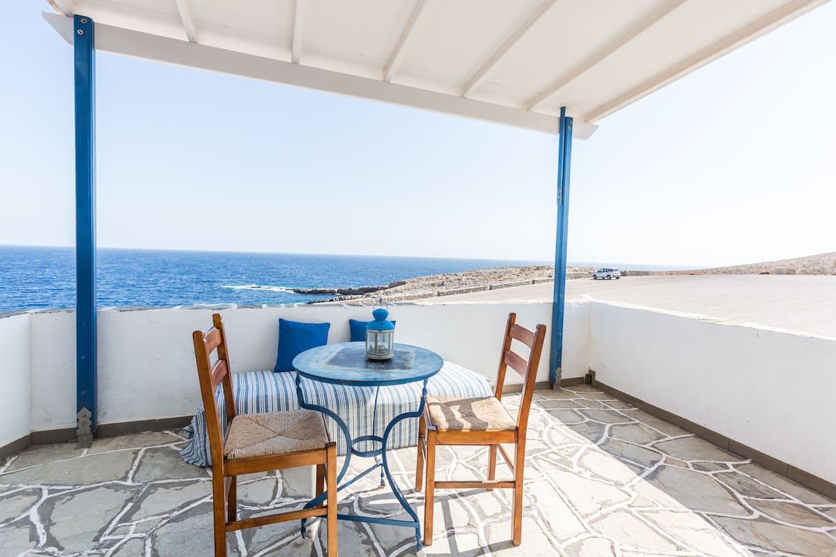 Une terrasse avec une table et des chaises, donnant sur une plage et la mer.
