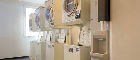 A row of front-loading washing machines in a laundry room with a window and a water dispenser.
