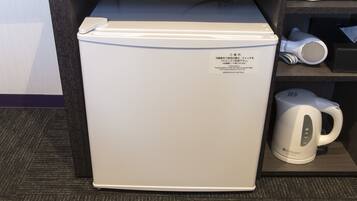 A compact refrigerator with a label, a hairdryer, and a kettle on a shelf.