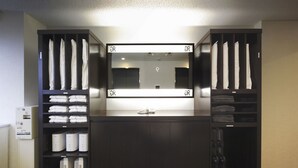 Habitación de hotel con escritorio central, espejo y repisas con toallas dobladas y batas.