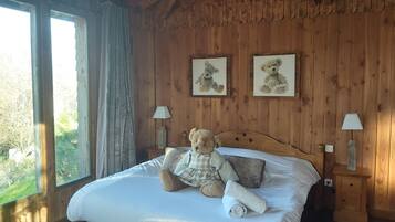 Ein Zimmer mit Holzboden, einem Bett, zwei gerahmten Bildern, einem Teddybären und einer Lampe.