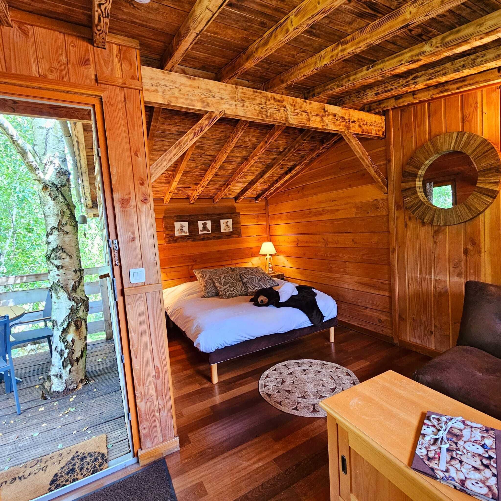 A cozy wooden cabin room with a bed, a small table, and a door leading outside.