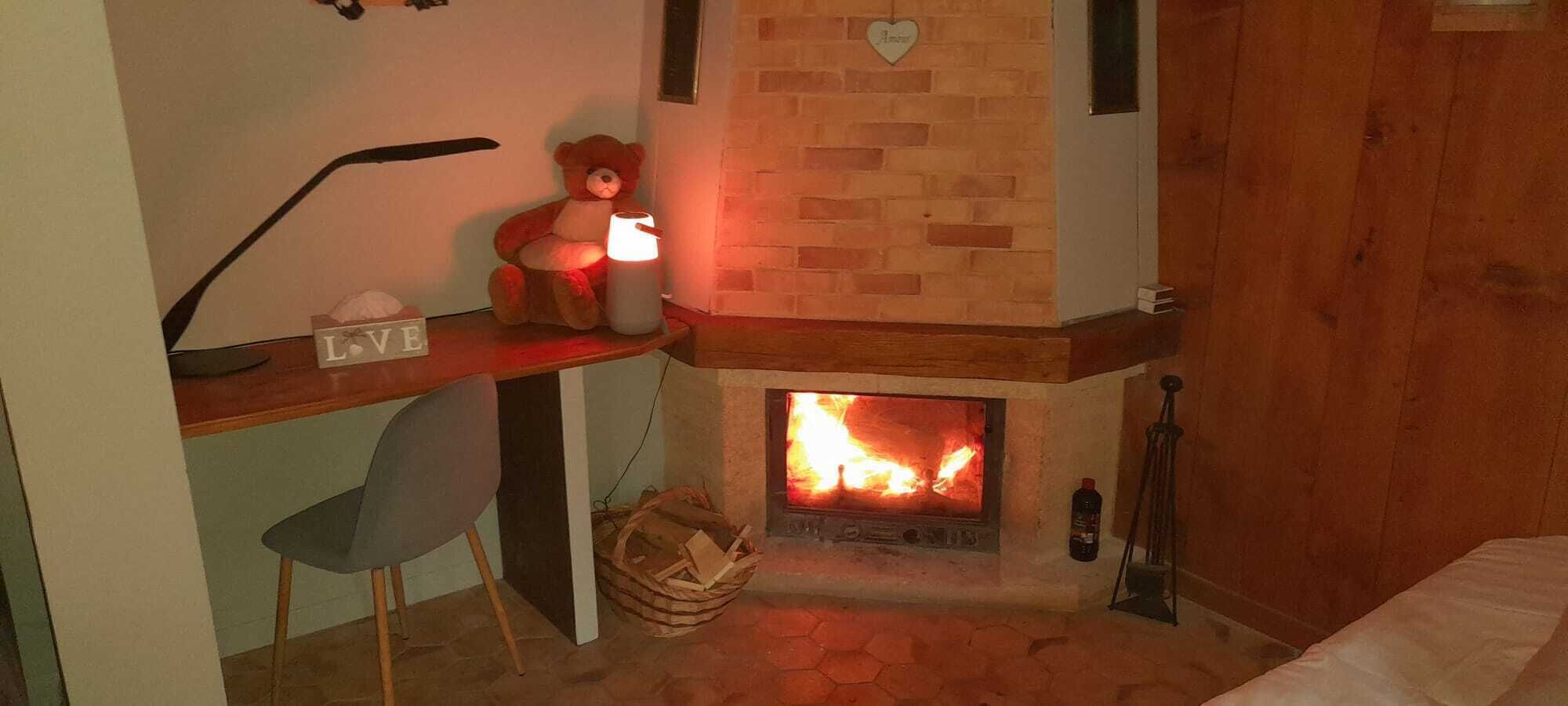 Una habitació acollidora amb una llar de foc, un escriptori amb un os de peluix i una cadira.