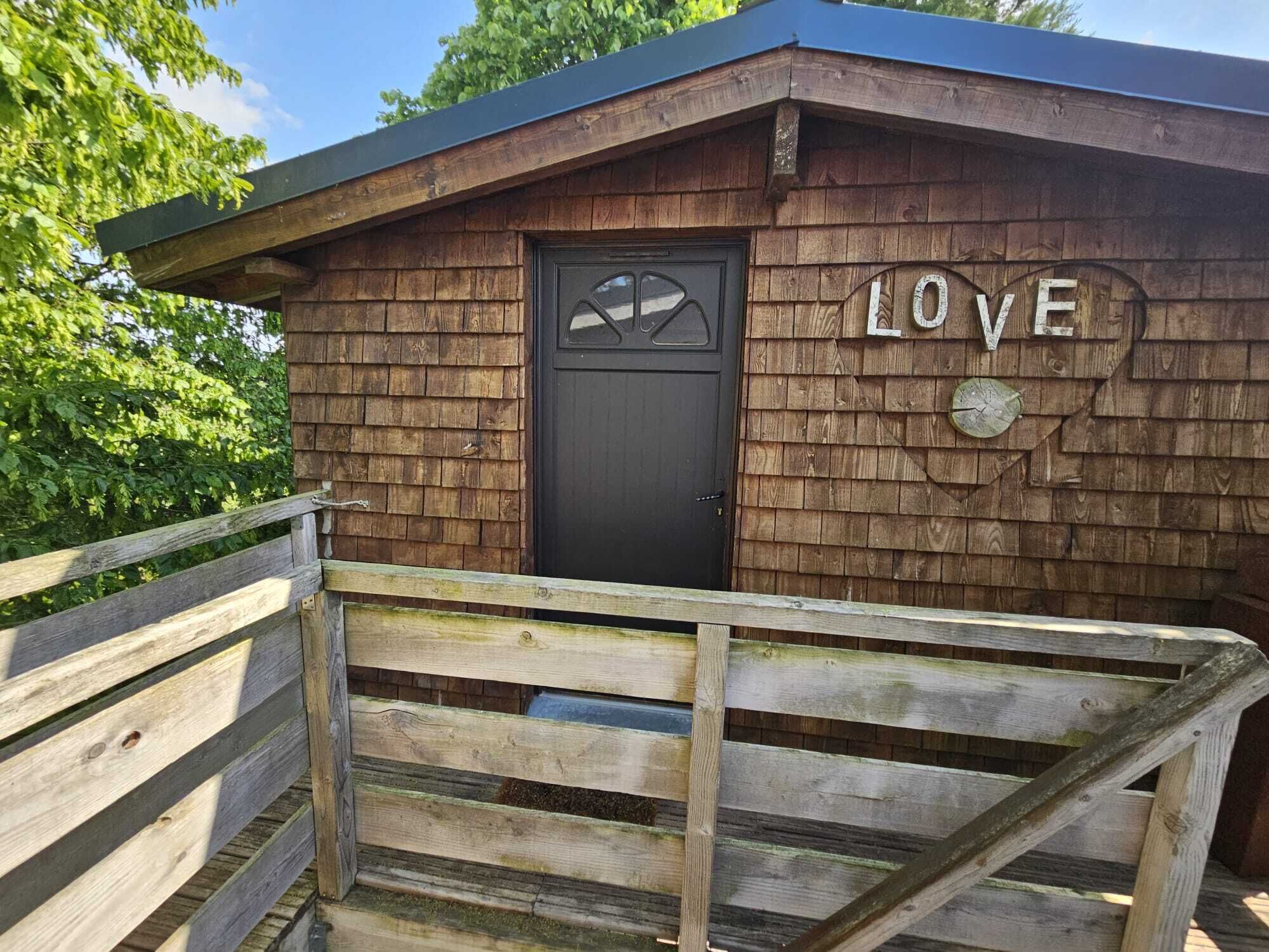 A wooden cabin with a black door and a 'LOVE' sign on the wall.